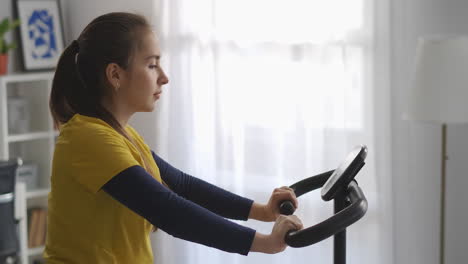 young-woman-is-training-with-spinning-bike-in-home-medium-portrait-of-sporty-lady-panoramic-in-living-room-healthy-lifestyle-and-good-physical-condition
